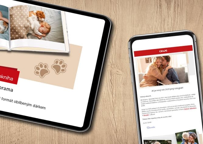 Tablet s otevřenou fotoknihou zobrazující dítě spící se psem, vedle něj je mobilní telefon s otevřeným e-mailem na dřevěném stole <p>CEWE newsletter</p>