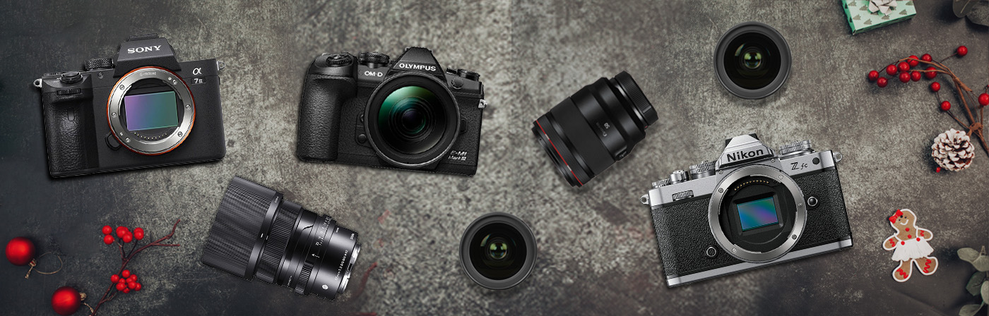 Foto čtyř fotoaparátů značek Sony, Olympus a Nikon s několika objektivy, položených na šedém pozadí s vánočními dekoracemi