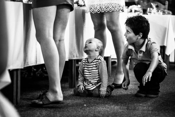 Malé dítě sedící na podlaze a hledící vzhůru vedle stojícího dítěte a dospělých žen.